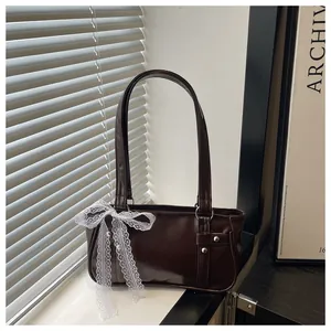 Detail of chocolate leather underarm bag featuring a large white lace bow and rivet decor