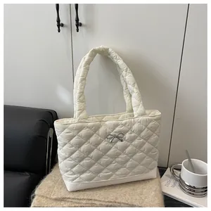 Detail view of a white quilted tote bag featuring a silver metal bow and soft texture