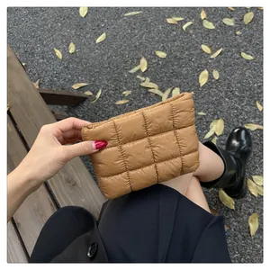 Nahaufnahme einer braunen gesteppten Puffer-Clutch auf einer Bank mit Herbstblättern