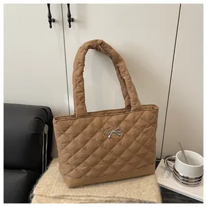 Close-up of brown quilted tote bag with silver bow detail on soft beige texture