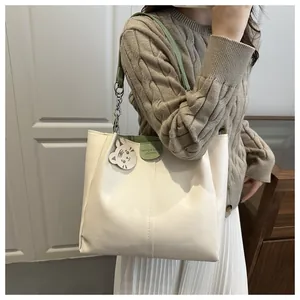 Close-up of cream and green tote bag featuring metallic chains and a cute cat charm
