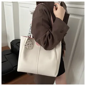 Detail view of large cream tote bag with pink straps and cute animal charm on a sofa