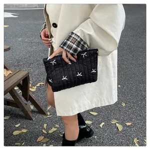 Detail einer schwarzen gesteppten Handtasche mit weißer Stickerei, von einem Model gehalten