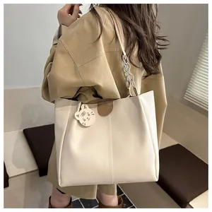 Detail of off-white tote bag with decorative stitching, chain strap and cat charm