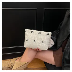 Detail der weißen gesteppten Nylon-Clutch mit schwarzer Schleifenstickerei und Reißverschluss