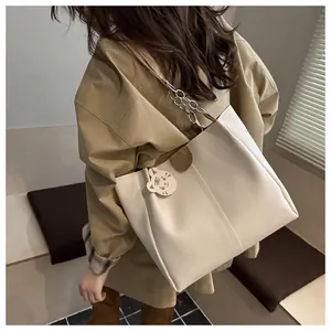 Detail view of large cream leather tote bag with metal chain strap and cat charm