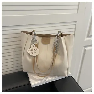 Detail of cream tote bag with tan handles and white cat charm on a stack of books