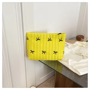 Detail der gelb gesteppten Clutch-Tasche mit schwarzen Schleifen und Reißverschluss