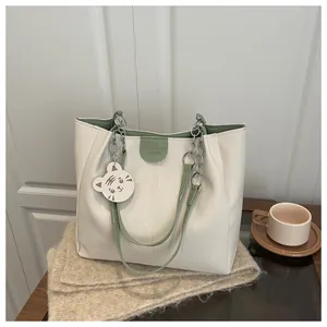 Detail of cream tote bag with green leather trim, chain strap, and cute tiger charm
