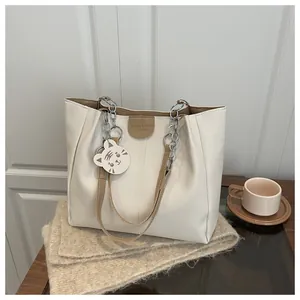 Detail of beige tote bag with brown straps, silver chain, and cute cat charm pendant