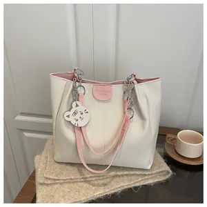 Detail of cream tote bag with pink straps, metallic chain, and cute tiger charm