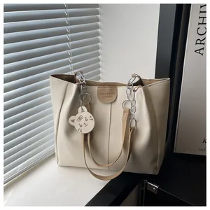 Detail of cream tote bag with thin brown straps and silver chain, featuring a cute tiger charm