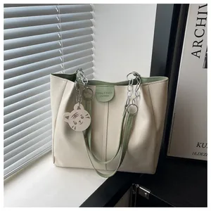 Detail of cream tote bag with green handles, silver chain strap, and tiger charm