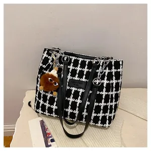 Close-up of black and white checkered tweed tote bag with leather logo and chain strap