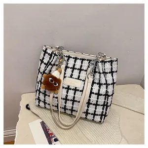 Detail of checkered tweed tote bag texture with leather logo patch and plush charm