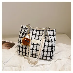 Detail of checkered tweed tote bag with leather straps and cute plush monster charm