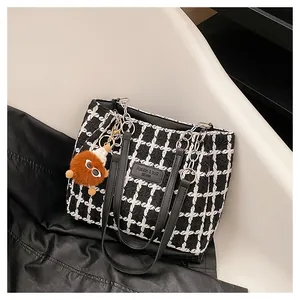 Detail of tweed checkered tote bag with metal chain handles and brown plush charm