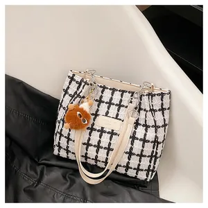 Macro detail of black and white tweed tote bag featuring leather chain straps and logo