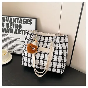 Detail of black and white plaid tweed tote bag featuring leather straps and plush charm