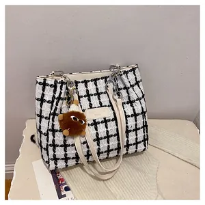 Detail of checkered tweed tote bag featuring a plush ball charm and a vintage leather patch