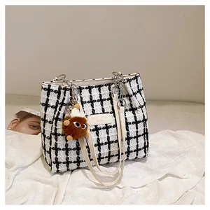Detail of tweed checkered tote bag with chain strap and cute monster plush pendant