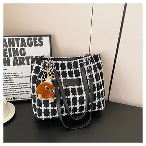 Close-up of black and white plaid tweed tote bag with plush charm and chain strap