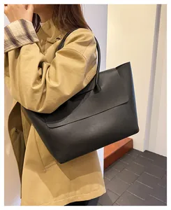 Detail of black leather tote bag with grainy texture worn with a khaki trench coat