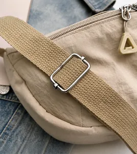 Detalle de correa de nailon beige ajustable con hebilla de metal plateado y tirador de cierre