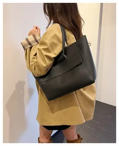 Detailed side view of large black leather tote bag worn by model in minimalist studio