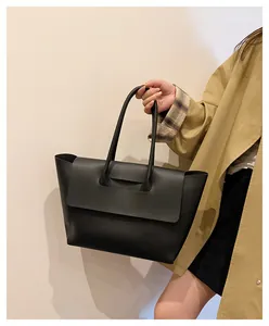 Detail of the black leather tote bag showing the unique flap closure and long shoulder strap
