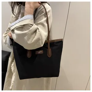 Close-up of black tote bag with brown leather straps and branded logo patch detailing