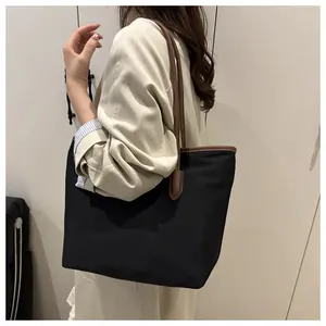 Close-up of a large tote bag with black fabric and brown leather trim on the shoulder