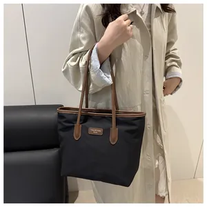 Detail of a large black tote bag with brown leather handles and brand logo tag