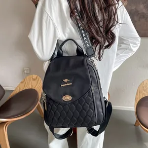 Rear view of a black quilted backpack with gold hardware worn by a model in a minimalist room