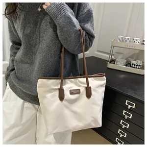 Detail of cream tote bag with brown leather handles and brand logo patch for daily commute