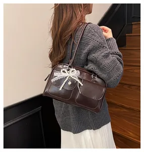 Detail of dark brown leather pillow bag featuring lace bow, pearl charm, and double pockets