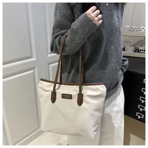 Detailed shoulder view of a cream nylon tote bag with brown leather trim and branding