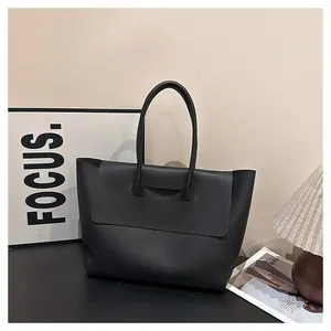 Detail of a large black leather tote bag with flap closure and elegant round handles