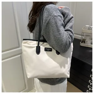 Close-up of beige tote bag with black straps and branded leather patch detail