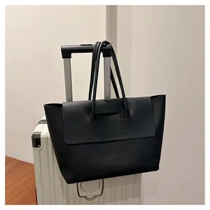 Black matte leather tote bag attached to luggage handle for convenient travel commute