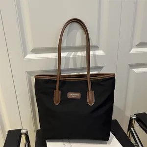 Large black tote bag with brown leather handles and logo on a minimalist background