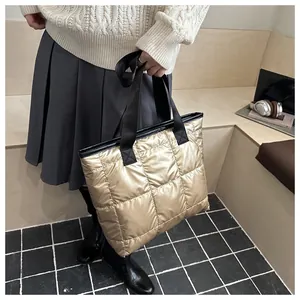 Detalle de bolso tote acolchado dorado con correa negra y acabado metálico brillante