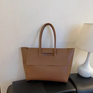 Brown large capacity commuter tote bag with flip buckle closure on a leather bench