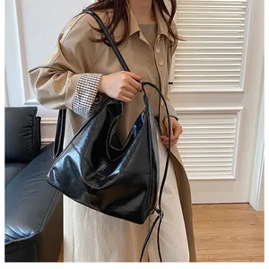 Detail of glossy black leather tote bag showing a sleek half-moon fold on beige trench coat