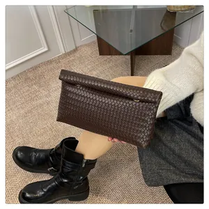 Detail of a dark brown woven leather clutch held by a model in a stylish indoor setting