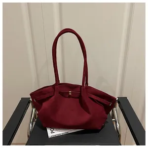 Detailed close-up of burgundy suede tote bag with golden hardware on a modern chair