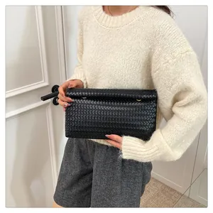 Detail of woven black leather clutch with golden clasp held by a woman in casual attire