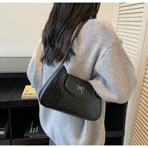 Détail d'un sac d'épaule noir brillant à motif crocodile avec nœud argenté