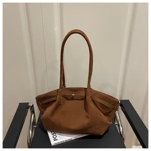 Close-up of brown matte suede tote bag with metal bow buckle on a minimalist chair