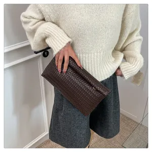 Detail of a dark brown woven leather clutch held by a model in casual attire